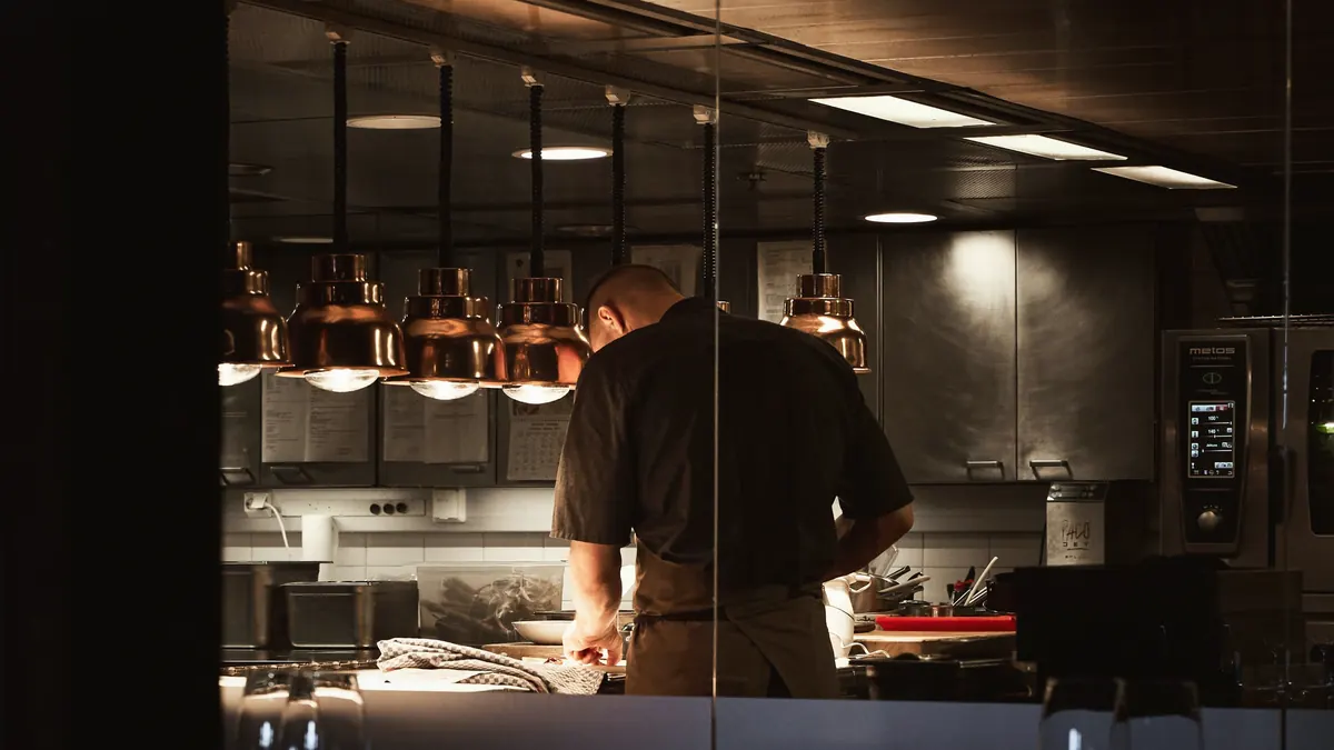 kok aan het werk in de open keuken, onder koperen lampen